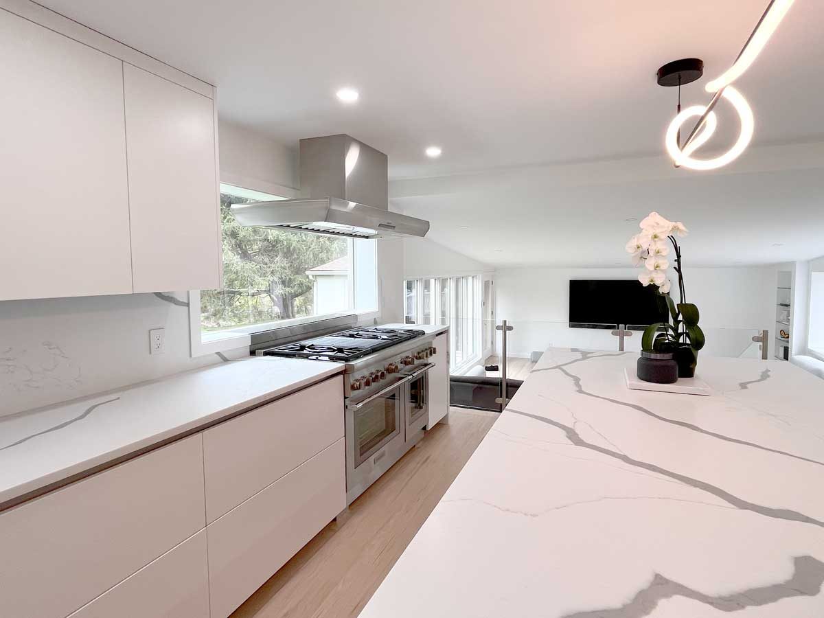 Kitchen remodeling project featuring sleek flat-front white cabinets, quartz waterfall island, professional stainless steel range, steel hood vent, and modern LED pendant light.