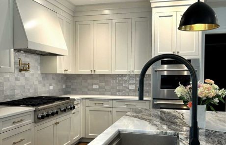 White shaker kitchen remodel with marble island countertop, undermount stainless steel sink, black matte faucet, stone tile backsplash, and stainless steel appliances.
